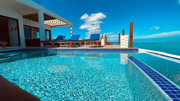 A clear blue pool with lounge chairs, a wooden deck, and a view of the ocean.