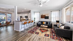 A modern living room with a sofa, coffee table, and a patterned rug. There is a kitchen area with a refrigerator and microwave. - Boho Bungalow - 30ft pool & minutes from festivals  (Indio)
