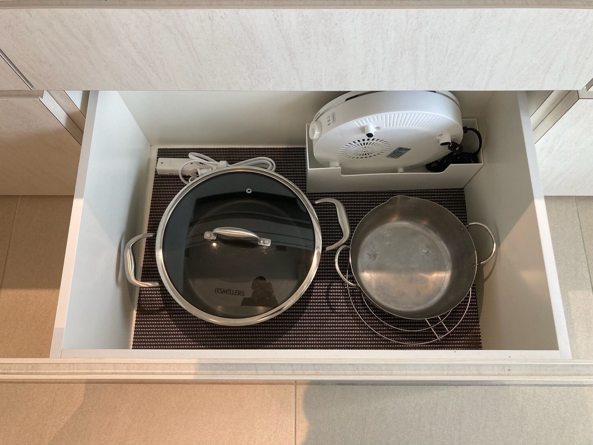 Un cajón de cocina con una olla, sartén y un electrodoméstico pequeño.