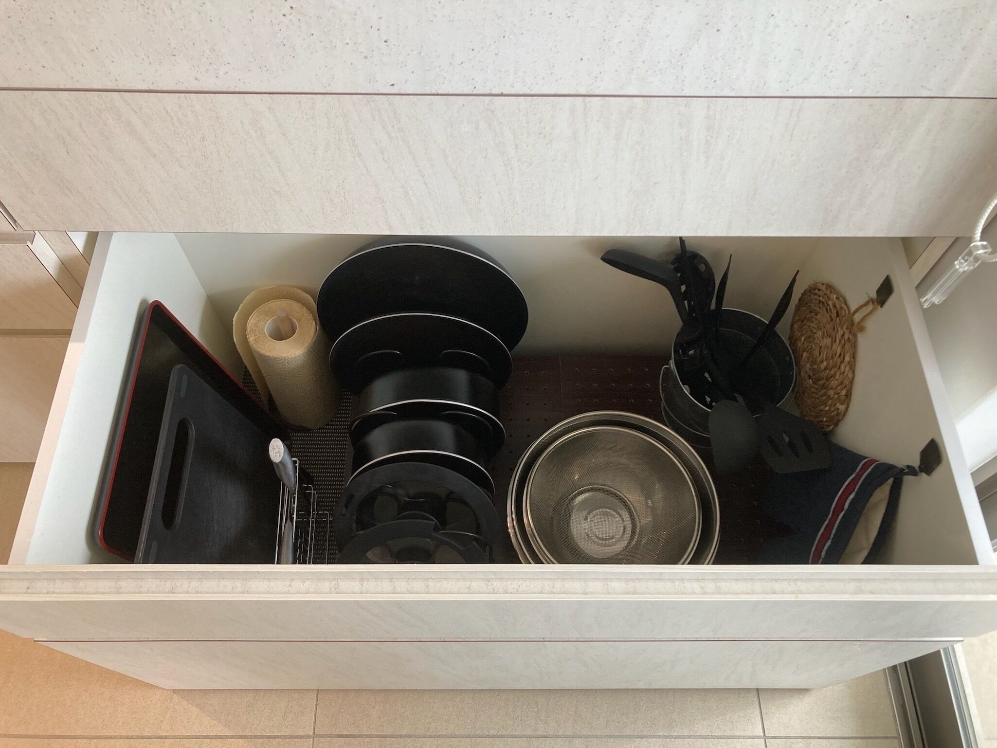 A kitchen drawer with various utensils and cookware, including pots, pans, and a strainer.