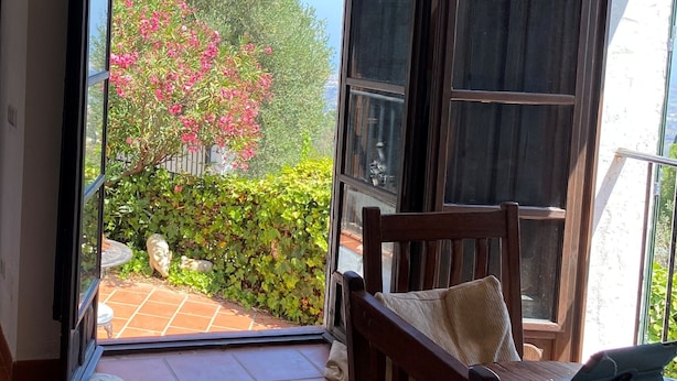 A room with a large sliding glass door leading to a balcony with a view of a garden and a tree with pink flowers. - Spectacular Views Private Villa Valtocado (Mijas Pueblo)