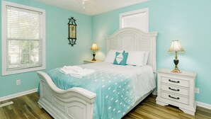 A bedroom with a bed, two bedside tables, a ceiling fan, and a window with blinds. - PRIVATE Pool w/ Lithium  Golf Cart w paid parking INCLUDED. Walk to Restaurants (Oak Island)