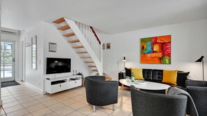 Ein modernes Wohnzimmer mit Fernseher, grauen Sofas, einem Esstisch und einer Treppe.