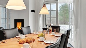 Ein Esszimmer mit Holztisch, gedeckt für vier Personen, Kamin und großen Fenstern mit Blick auf Bäume.