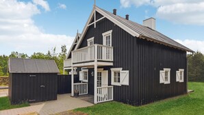 Ein zweistöckiges, schwarzes Holzhaus mit Balkon, einer kleinen Werkstatt und einem gepflasterten Auffahrt.
