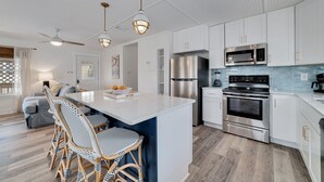 A modern kitchen with white cabinetry, stainless steel appliances, and a central island with bar stools. - Reel' Em Inn- A boater's paradise! (Orange Beach)