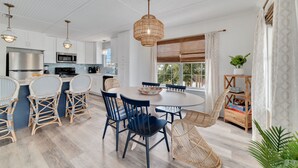A modern kitchen with white cabinetry, stainless steel appliances, and a dining area with wicker chairs and a round table. - Reel' Em Inn- A boater's paradise! (Orange Beach)
