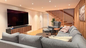 Un soggiorno moderno con un divano grigio, una TV montata a parete, una scala in legno e un piccolo tavolo con una sedia.