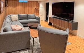 Un salon moderne avec un canapé d’angle gris, une petite table basse et un téléviseur posé sur un meuble en bois.