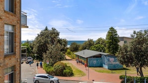 A coastal building with a view of the sea, surrounded by trees and a paved walkway. - Seaview 6 - Great Views in the Heart of Avoca (Avoca Beach)