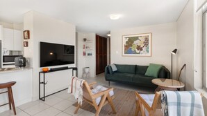 A compact living space with a kitchenette, a sofa, a coffee table, and a dining area. - Seaview 6 - Great Views in the Heart of Avoca (Avoca Beach)
