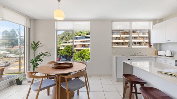 A modern kitchen with a dining area, large windows, and a view of a residential area. - Seaview 6 - Great Views in the Heart of Avoca (Avoca Beach)