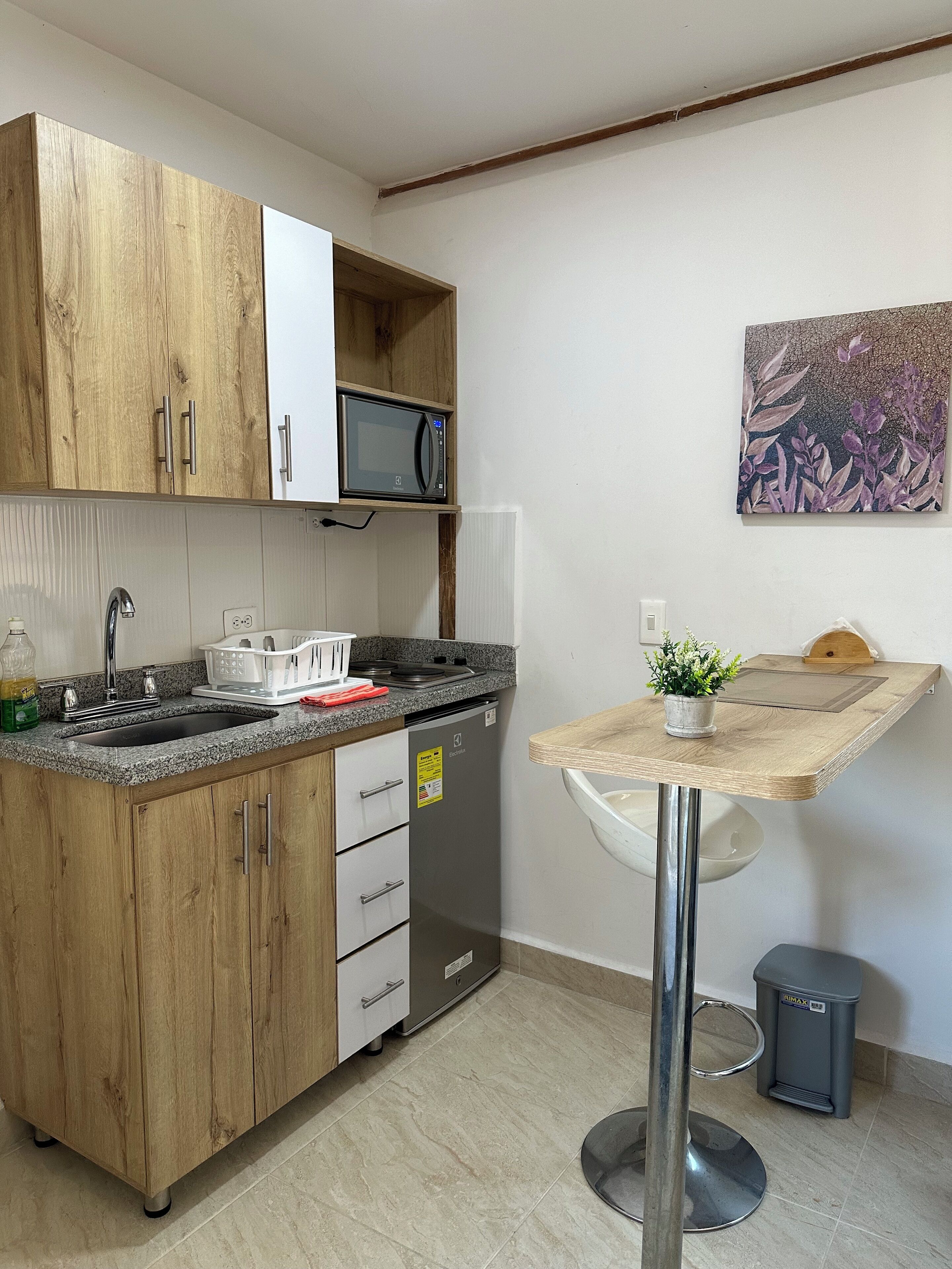 A compact kitchen with wooden cabinets, a built-in microwave, a sink, and a small dining table with a potted plant.