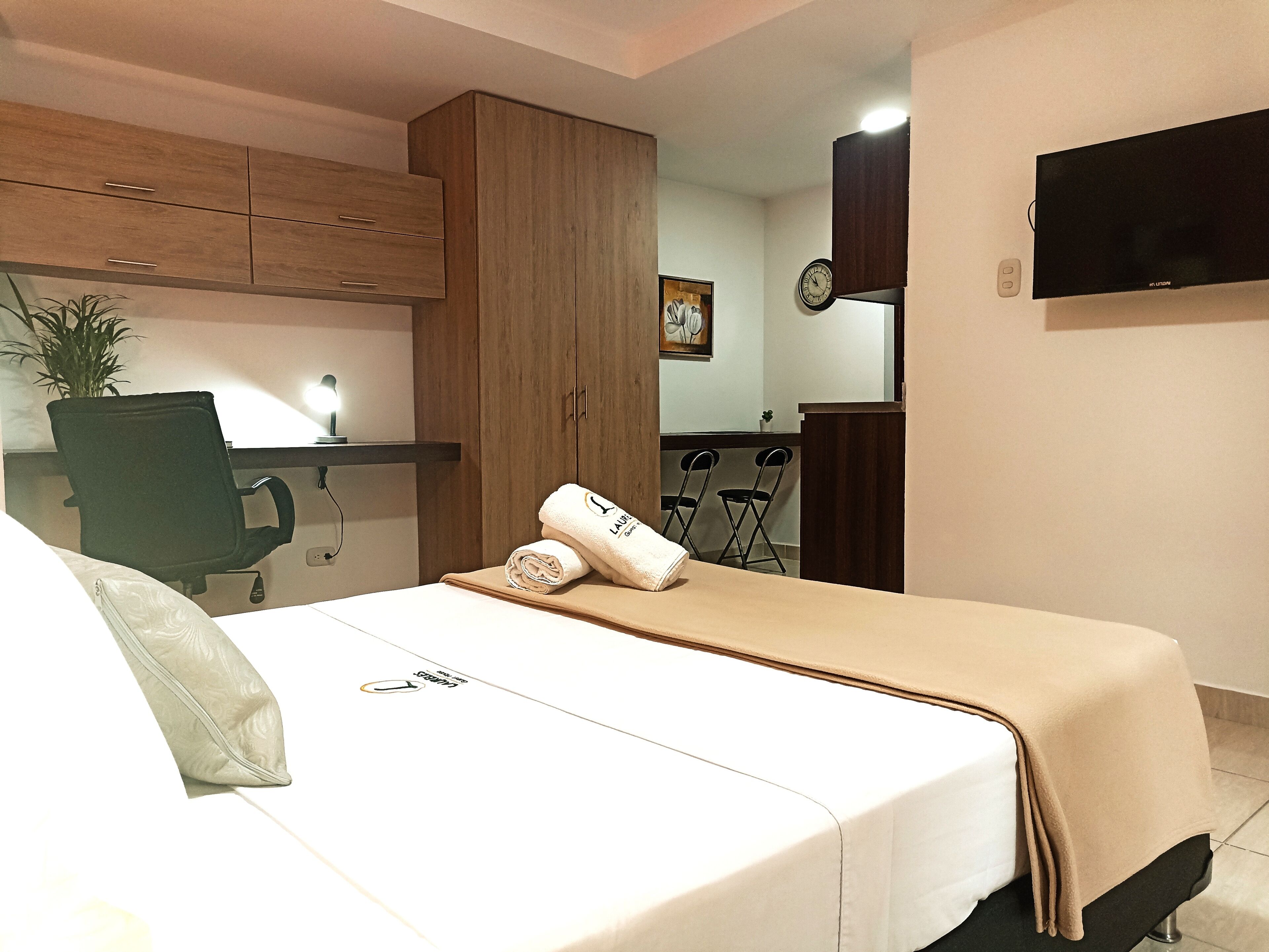 Una habitación de hotel con una cama, un escritorio con silla, un televisor y una kitchenette.