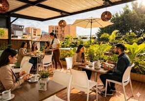 An outdoor café with tables and chairs, surrounded by potted plants and a view of buildings. - Laureles Grand House LGH Hotel - Anteriormente Laureles Guest House (Medellín)
