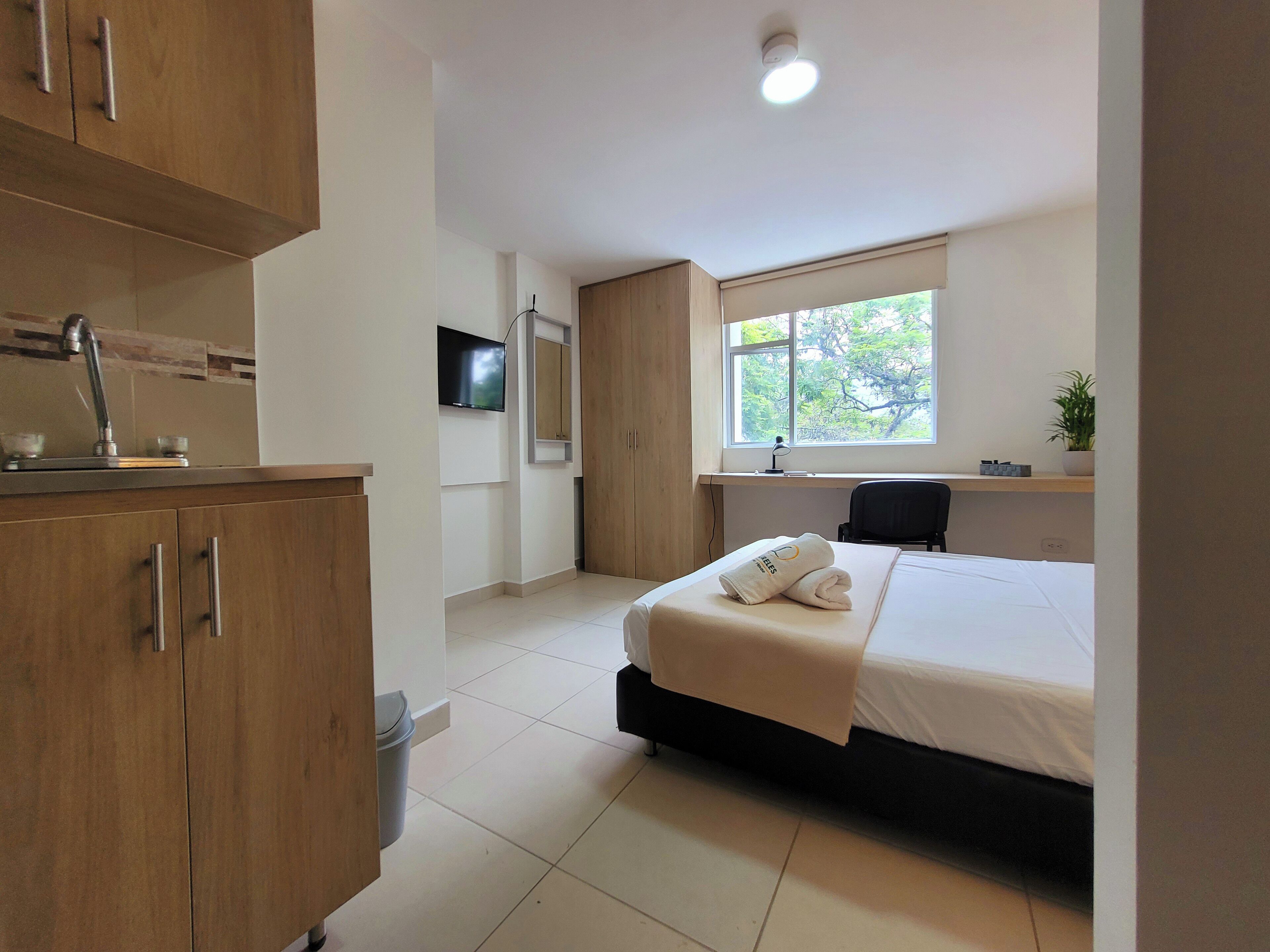 A modern bedroom with a bed, a desk, a TV, and a window.