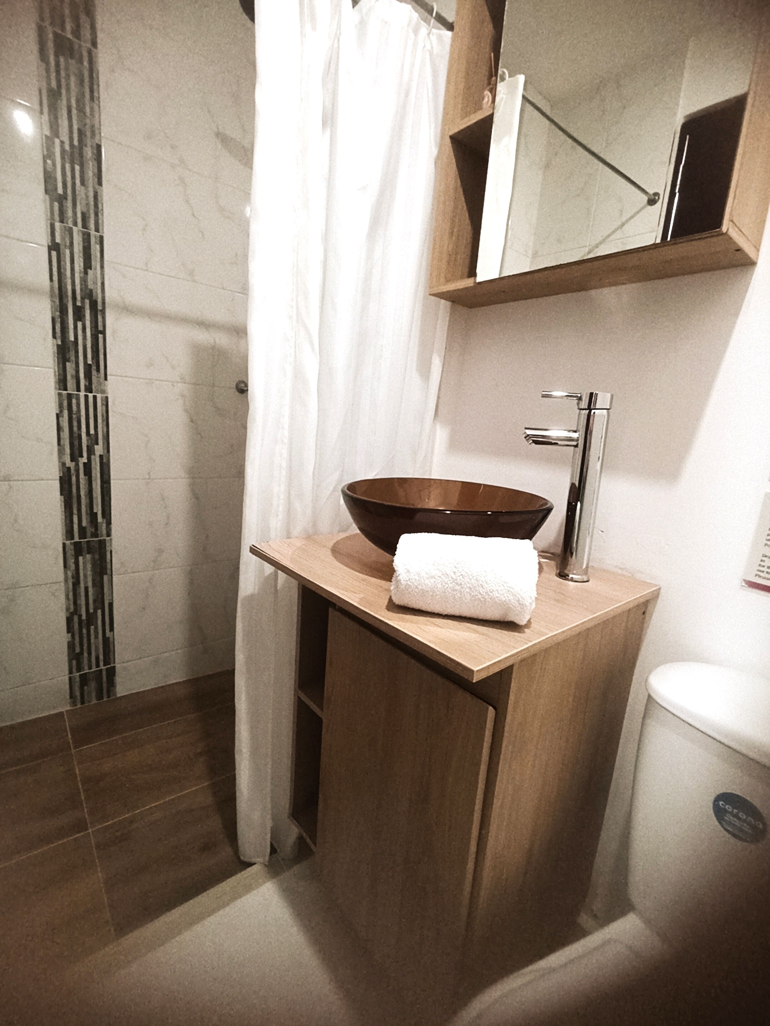 Een moderne badkamer met een houten wastafelmeubel, een grote spiegel en een douchecabine van glas.