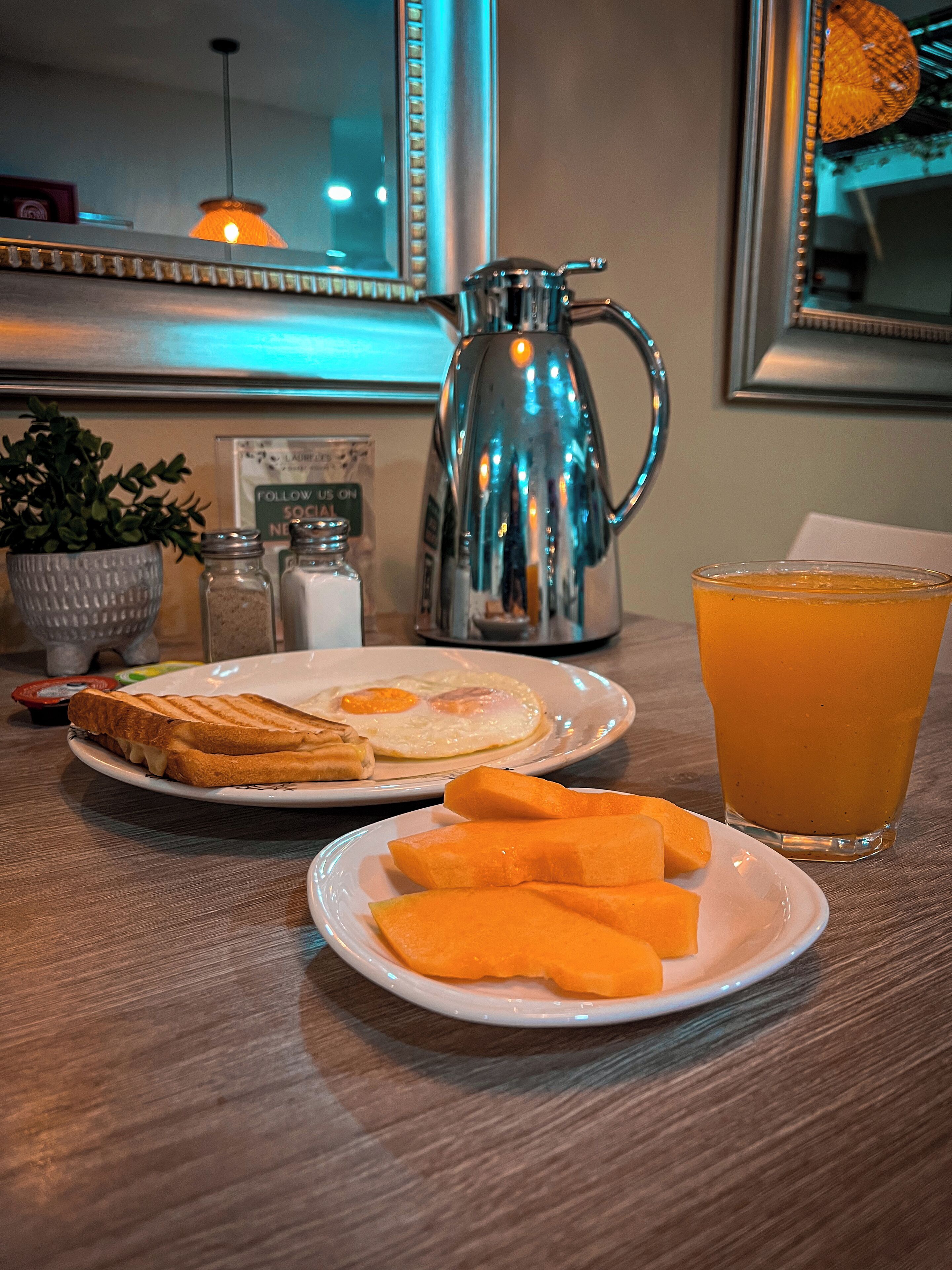 Une table en bois dressée pour le petit-déjeuner, avec des toasts, des œufs et un verre de jus d’orange.