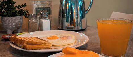 Une table en bois dressée pour le petit-déjeuner, avec des toasts, des œufs et un verre de jus d’orange.