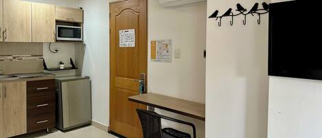 A compact kitchen with wooden cabinets, a microwave, a refrigerator, and a small dining table with a chair.