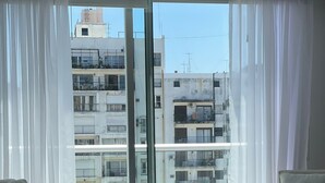 A modern bedroom with a large bed, two armchairs, and a view of a cityscape through floor-to-ceiling windows. - Studio β Super (Buenos Aires)