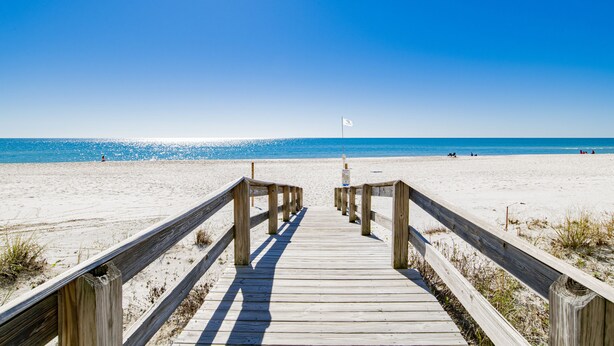 Een houten looppad dat naar een strand leidt, met een vlag in de verte.