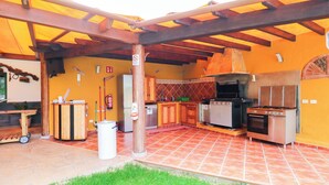 An outdoor kitchen with a grill, refrigerator, and wooden cabinets.