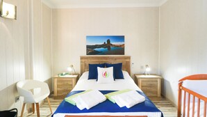 A hotel room with a bed, a chair, a crib, a nightstand, a lamp, and a painting on the wall.