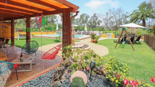 A covered patio area with outdoor seating, a pool, and a well-maintained garden.