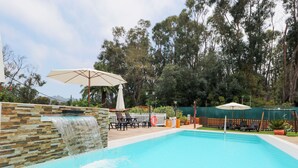 A swimming pool with a waterfall feature, surrounded by lounge chairs and umbrellas.