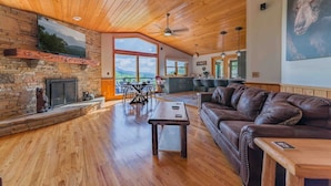A spacious living room with a stone fireplace, wooden ceiling, and large windows offering a view of the outdoors. - Location Location  Location ! Resort Pools , Hot Tub ! MILLION DOLLAR VIEW !! (Gatlinburg)