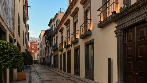 Una estrecha calle adoquinada flanqueada por edificios históricos con balcones y grandes puertas de madera.