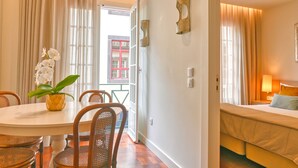 Habitación de hotel con cama, zona de comedor con mesa y sillas, y vista al exterior.