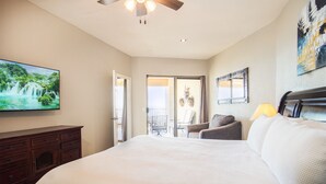 Un dormitorio con una cama grande, televisor en la pared, ventilador de techo y balcón con una silla.