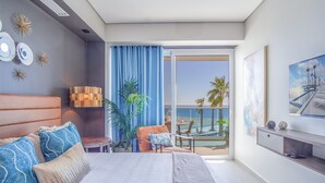 Une chambre d’hôtel moderne dotée d’un grand lit, d’un balcon avec vue sur la mer et d’un coin repas avec une table et des chaises.
