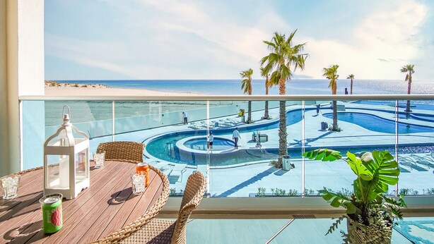 Un balcon avec vue sur un espace piscine, comprenant une piscine sinueuse et des palmiers.
