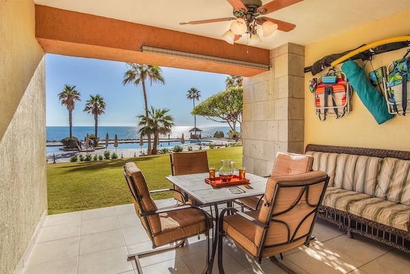 A patio with a table and chairs, a sofa, and a view of the ocean and palm trees.