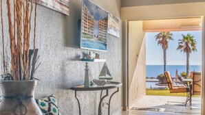 Una sala moderna con vista al océano, un comedor con mobiliario exterior y un ventanal grande que da al mar.