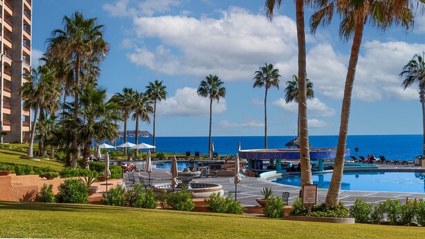 Un resort con zona de piscina, palmeras y vista al océano.
