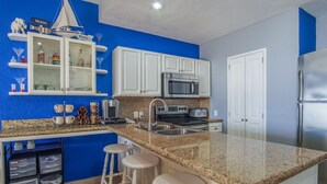 Una cocina con armarios blancos, encimera de granito, refrigerador de acero inoxidable y cafetera.
