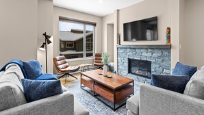 A modern living room with a stone fireplace, a flat-screen TV, and a large window offering a view of the outdoors.