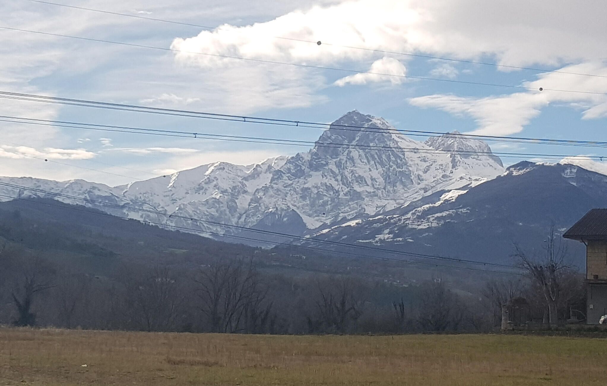 A mountain range with a prominent peak, power lines, and a building in the foreground.