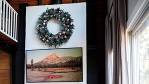 Een gezellige woonkamer met een open haard, een aan de muur bevestigd beeld van een berglandschap en een krans.