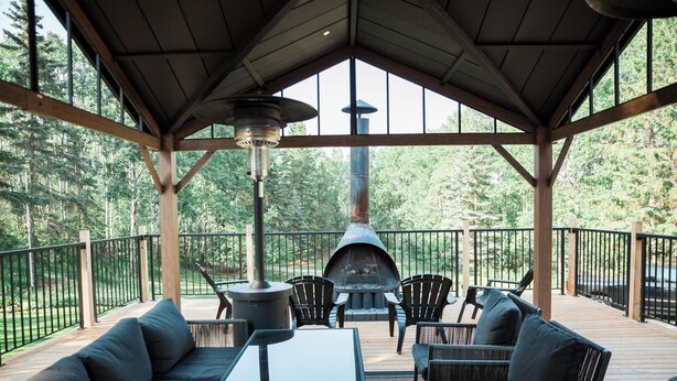 Een terras buiten met een ingebouwde vuurkuil, zitgedeelte en uitzicht op het omliggende bos.