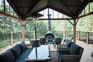 Eine Terrass mit eingebautem Feuerkorb, Sitzgelegenheiten und Blick auf den umliegenden Wald.