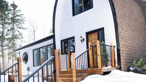 Een wit huis met een gebogen dak, een houten trap en een voortuin bedekt met sneeuw.