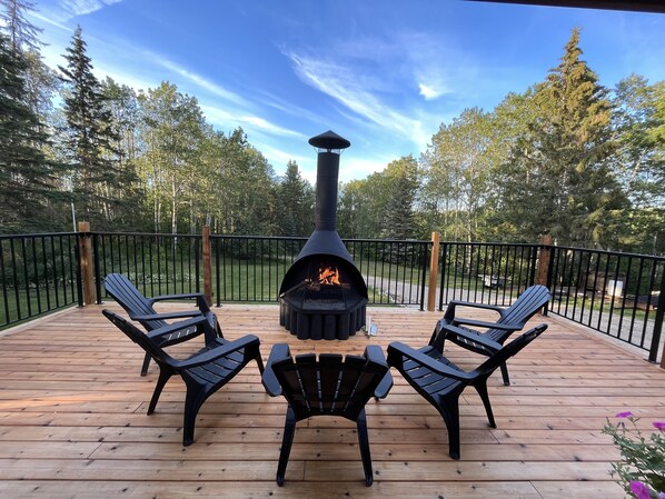 Eine Terrasse mit Kamin, vier Adirondack-Stühlen und einem Metallgeländer.