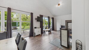 Une pièce spacieuse dotée de grandes fenêtres, d’un plafond en bois, d’un coin repas avec une table et des chaises, et d’un coin cuisine avec une cuisinière.
