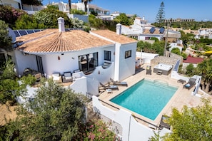A white villa with a tiled roof, a swimming pool, and a patio area with sun loungers.