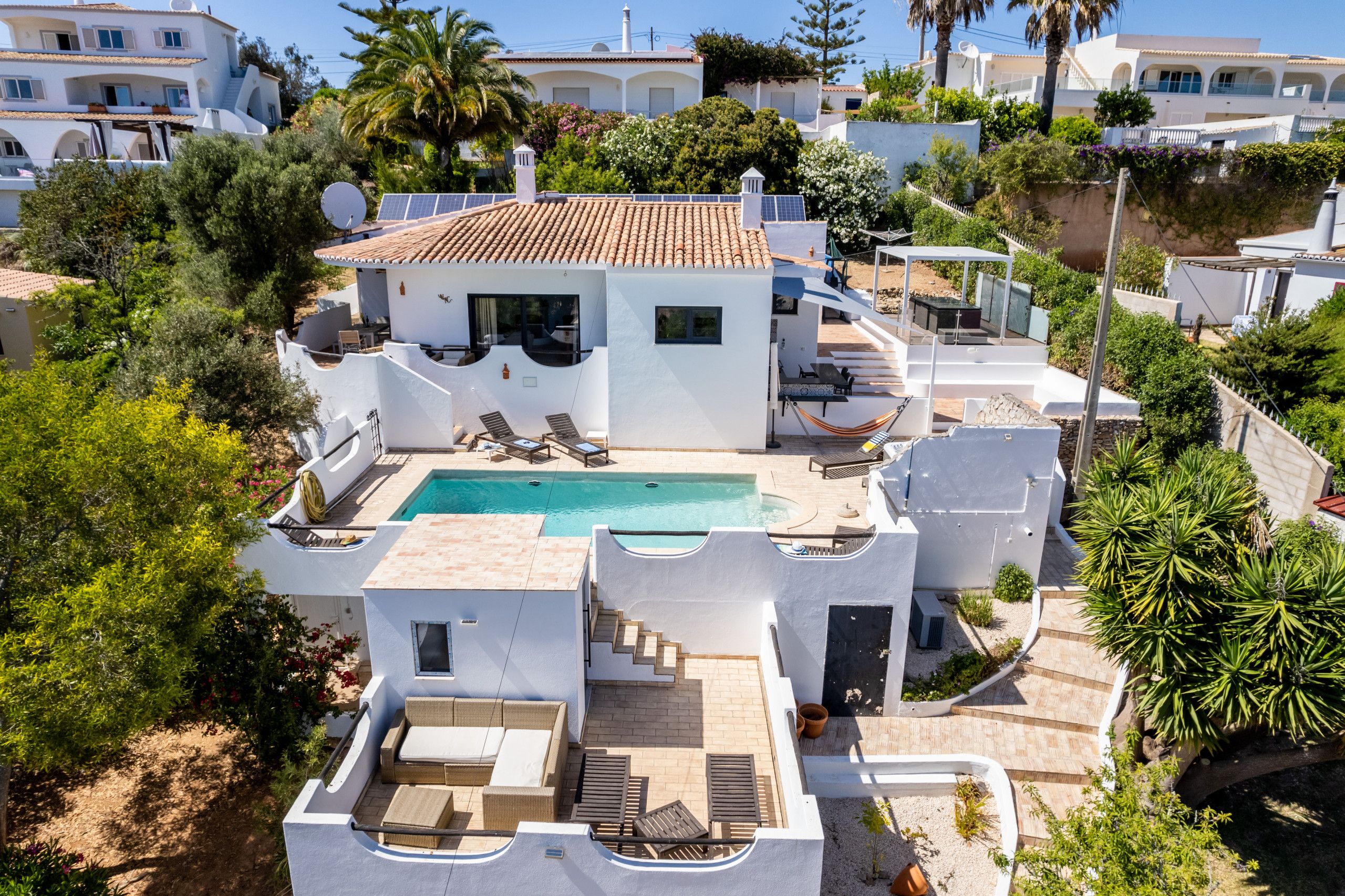 A modern villa with a swimming pool, outdoor seating, and a view of neighboring buildings.